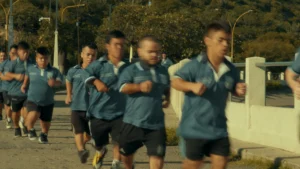 Argentinian men with dwarfism all have dark gray uniforms on. Their limbs are blurred as they are clearly running on a sidewalk, with trees in the background. 